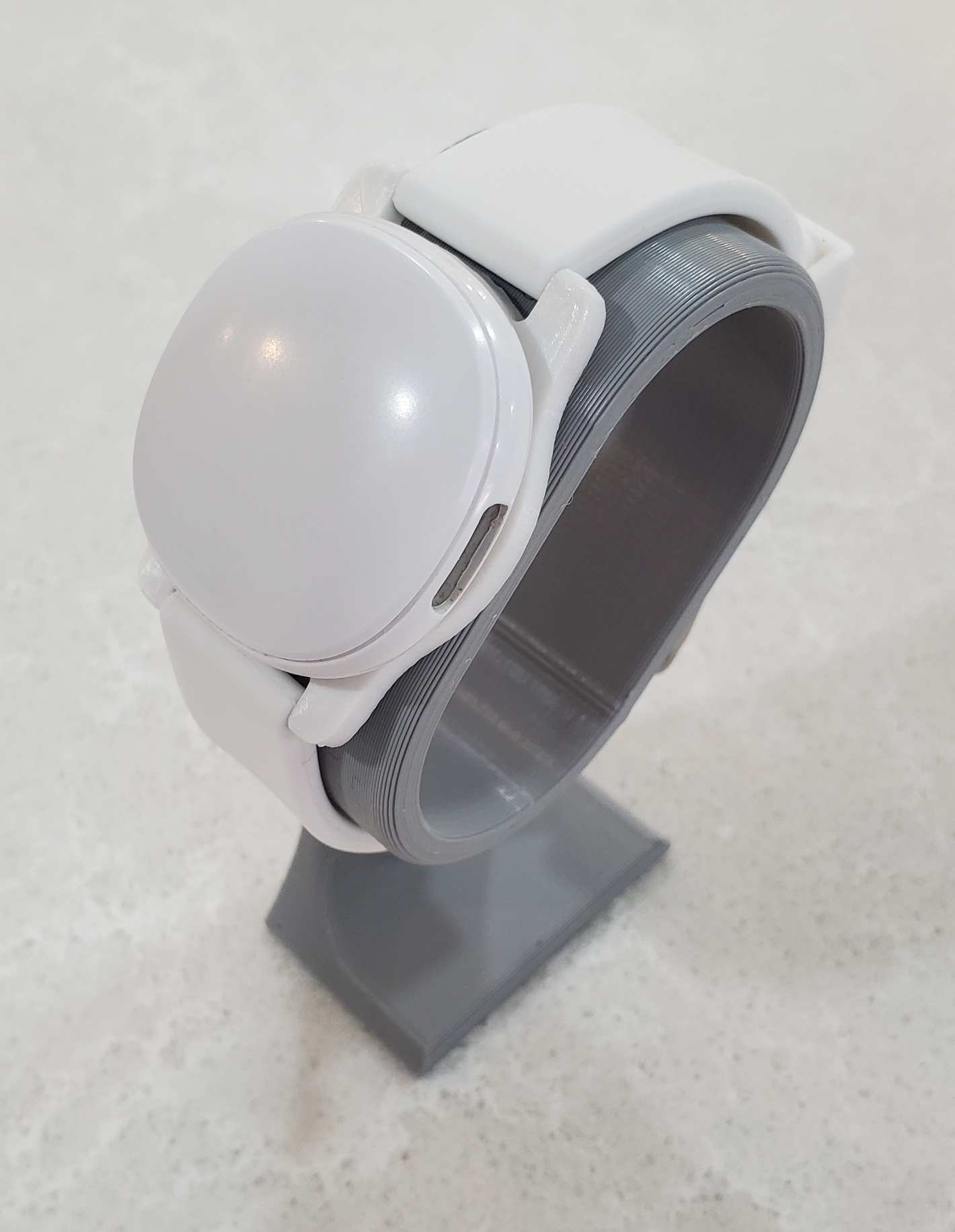 Ave Tracker mounted to Adapter and white silicone watch band, supported by gray watch stand